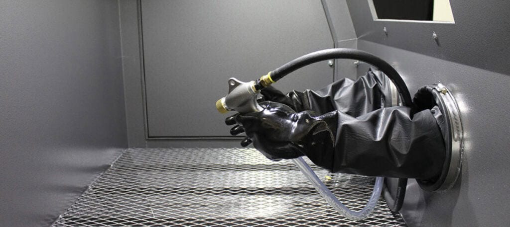 Operator holding blasting gun inside industrial manual sandblast cabinet