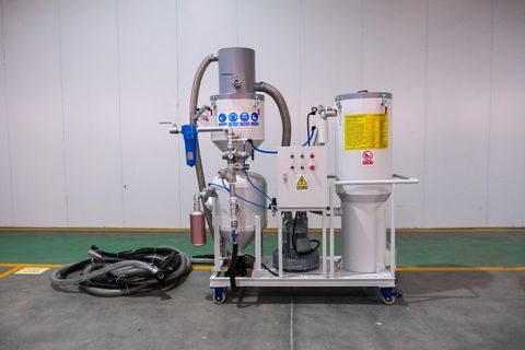 Sandblasting machine in an industrial setting, featuring a cyclone separator, electrical control panel, and dust collector system. The machine is equipped with hoses, safety labels, and controls for efficient abrasive blasting in surface preparation.