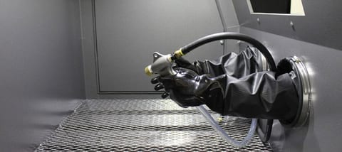 Operator holding blasting gun inside industrial manual sandblast cabinet