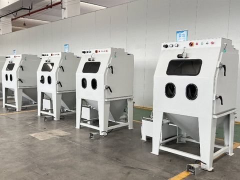 Row of white wet sand blasting machines in an industrial factory, featuring control panels and viewing windows.