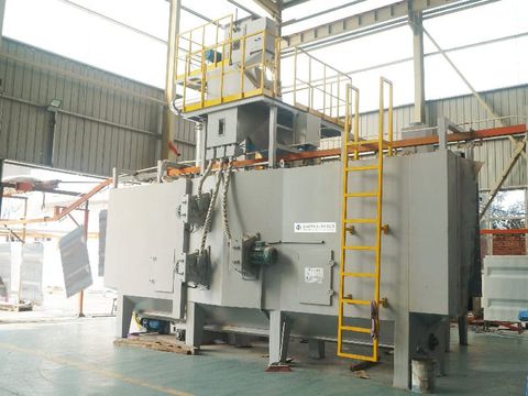 Industrial continuous hanger shot blasting machine with yellow safety features in factory setting